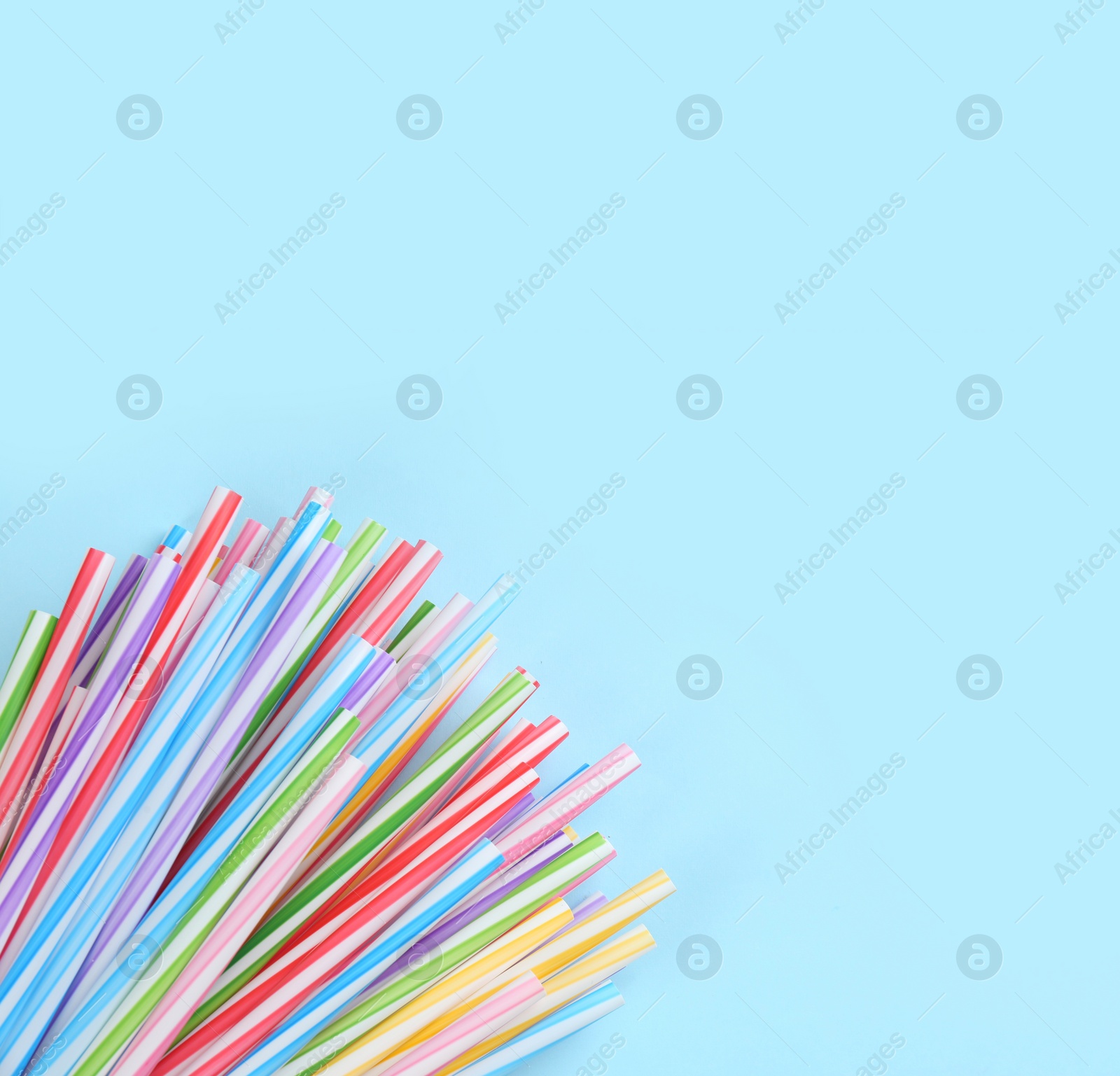 Photo of Heap of colorful plastic drinking straws on light blue background, flat lay. Space for text