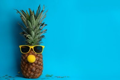 Pineapple with sunglasses and funny nose on light blue background, space for text. Creative concept