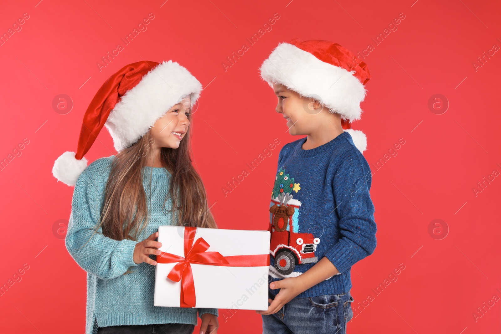 Photo of Happy little children in Santa hats with gift box on red background. Christmas celebration