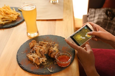 Photo of Woman playing game using smartphone at table with tasty BBQ wings in cafe, closeup