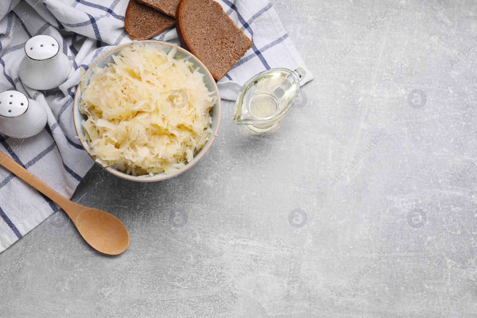 Photo of Bowl of tasty sauerkraut and ingredients on grey table, flat lay. Space for text