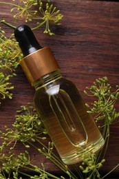 Bottle of essential oil and fresh dill on wooden table, flat lay