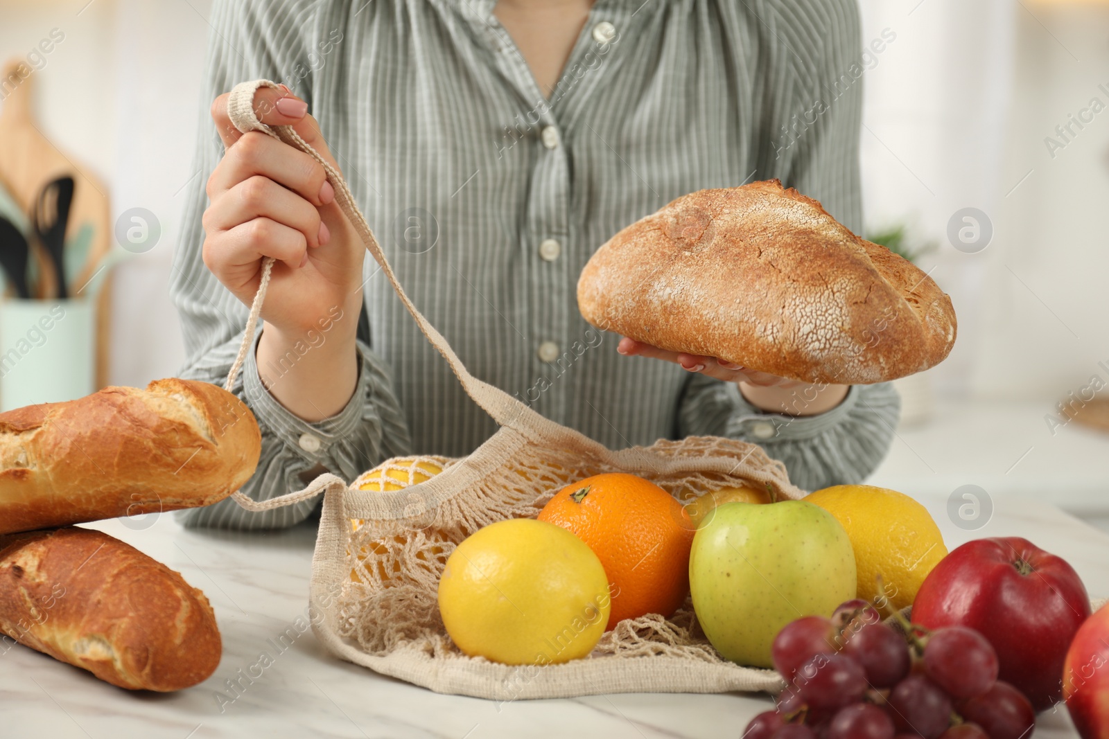 Photo of Woman with string bag of fresh fruits and bread at light marble table, closeup