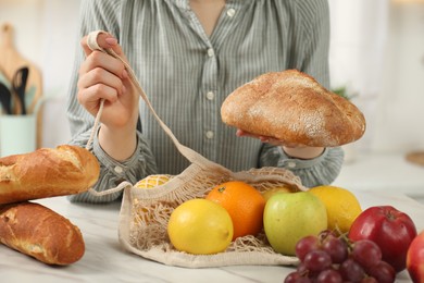 Woman with string bag of fresh fruits and bread at light marble table, closeup