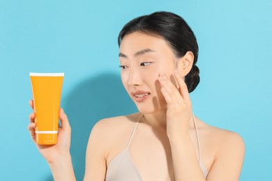 Photo of Beautiful young woman holding sun protection cream on light blue background