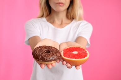 Photo of Woman choosing between doughnut and healthy grapefruit on pink background, closeup