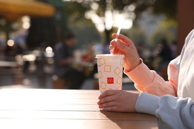 Photo of Lviv, Ukraine - September 26, 2023: Woman with McDonald's drink at wooden table outdoors, closeup. Space for text