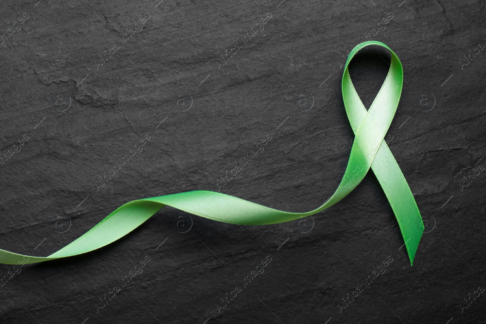 Photo of World Mental Health Day. Green ribbon on black background, top view with space for text