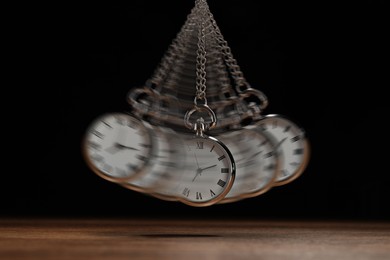 Image of Hypnosis session. Vintage pocket watch with chain swinging over wooden surface on black background, motion effect