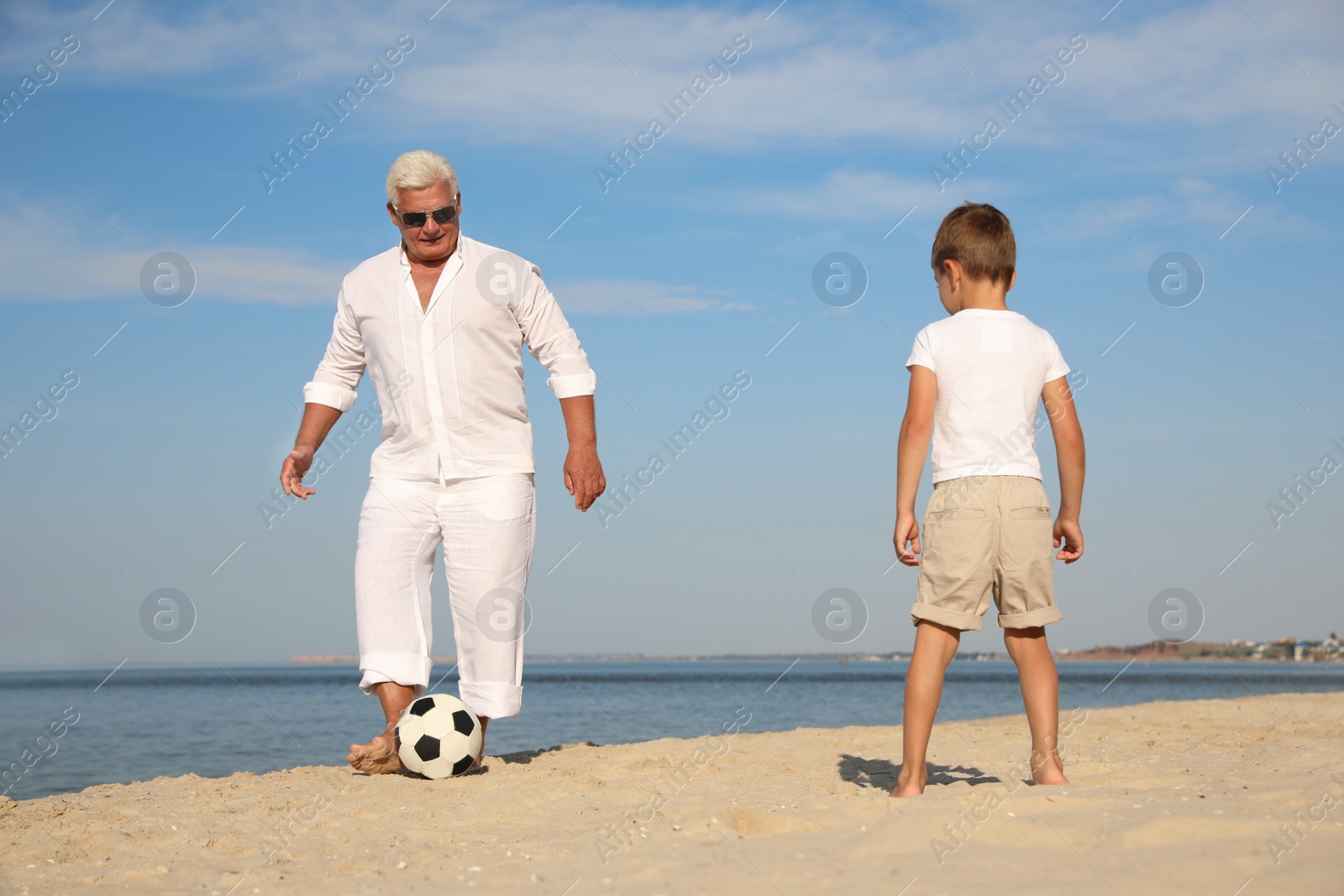 Photo of Cute little boy and grandfather playing with soccer ball on sea beach