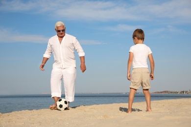 Cute little boy and grandfather playing with soccer ball on sea beach