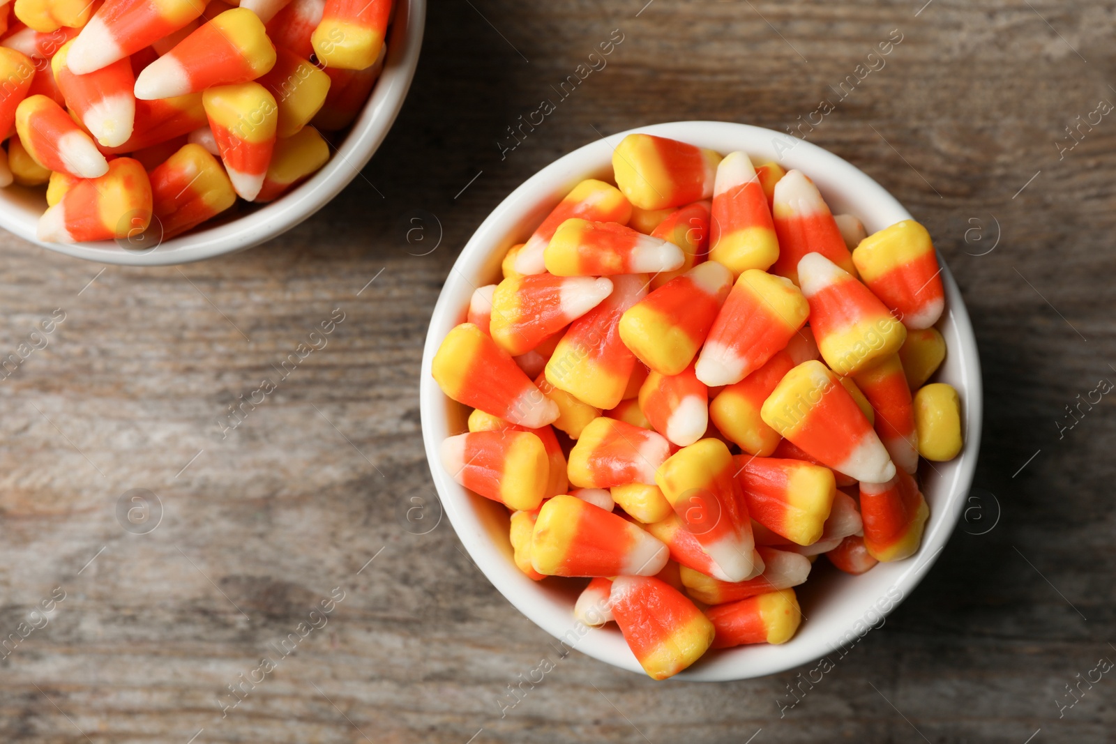 Photo of Bowl with tasty candy corns on wooden table, top view