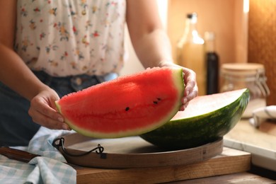 Photo of Woman holding slice of fresh juicy watermelon at wooden table, closeup