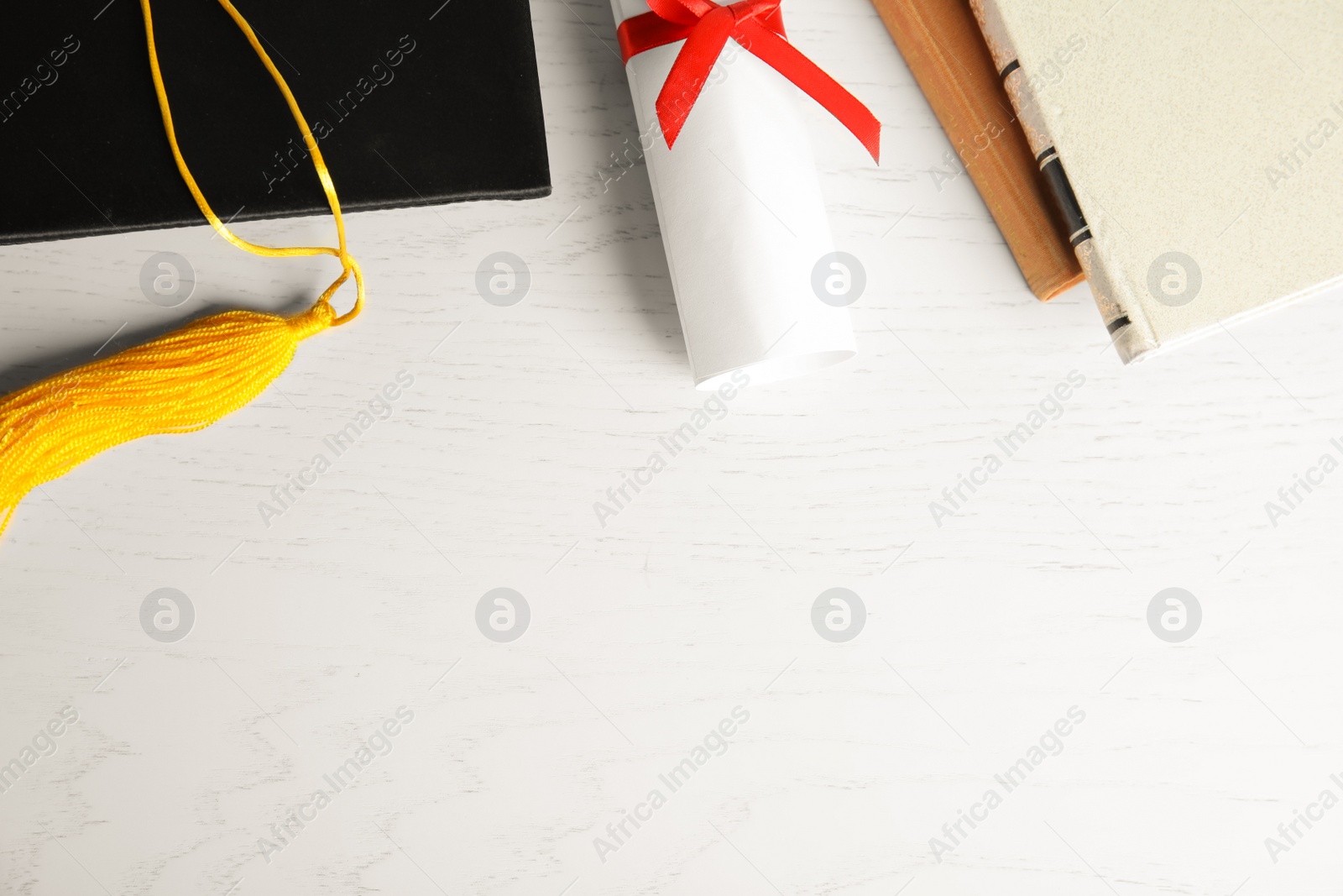 Photo of Graduation hat and student's diploma on white wooden table, flat lay. Space for text
