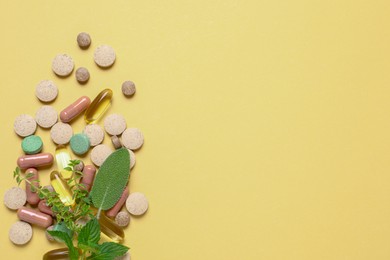 Different pills and herbs on light yellow background, flat lay with space for text. Dietary supplements