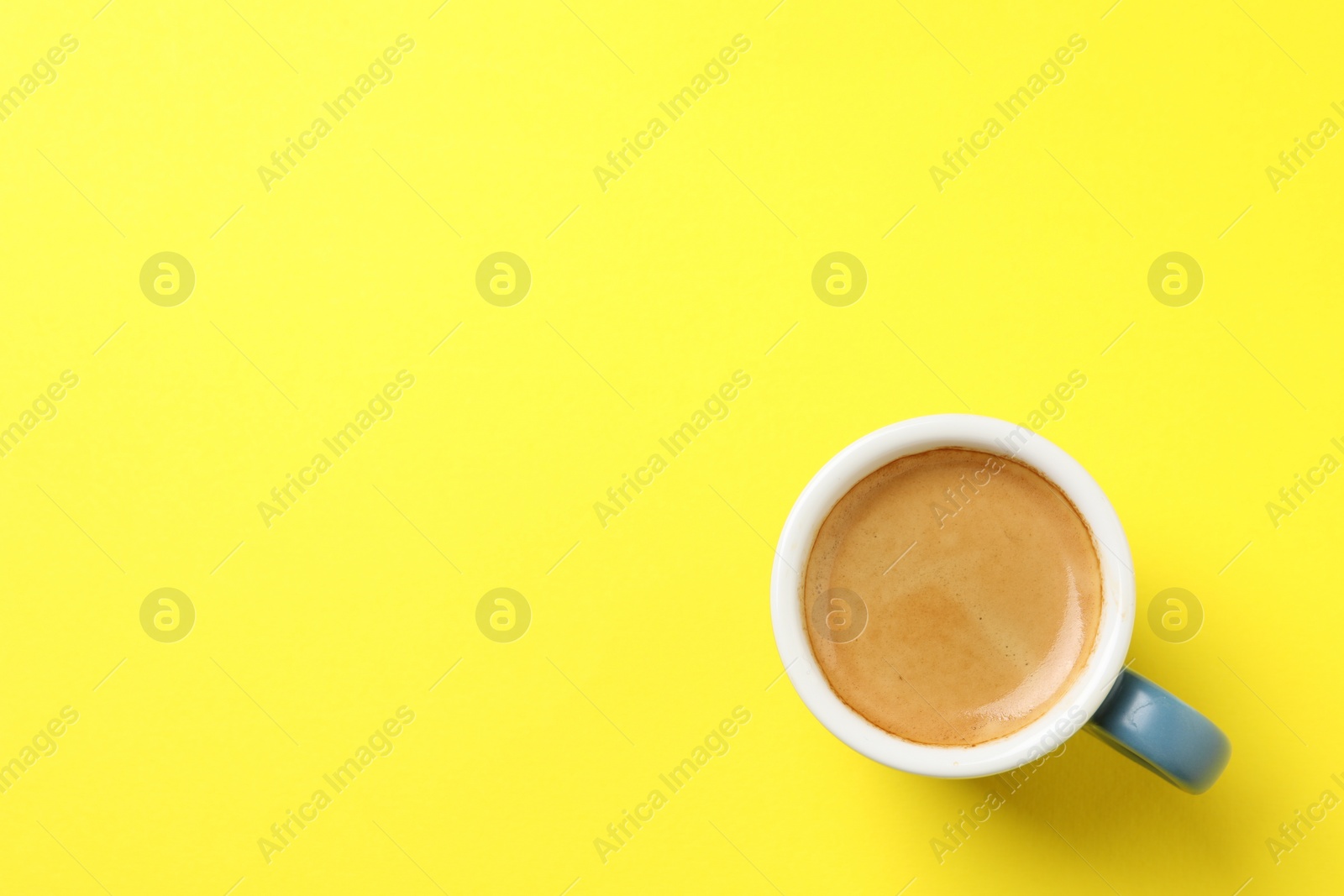 Photo of Aromatic coffee in cup on yellow background, top view. Space for text