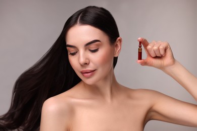 Photo of Beautiful young woman with long healthy hair holding ampoule on grey background