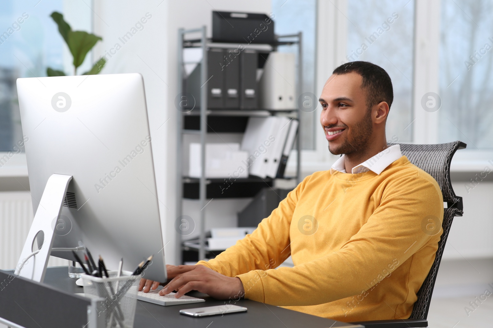 Photo of Young man working on computer at table in office