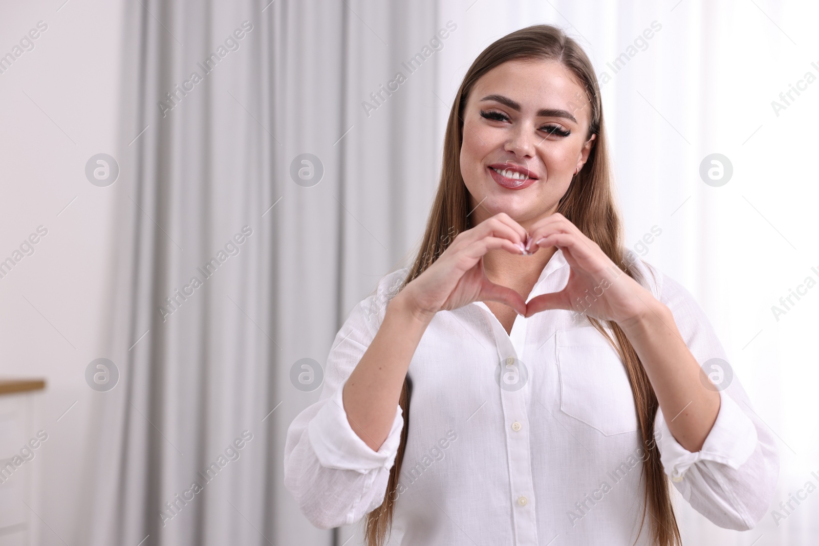 Photo of Happy woman showing heart gesture with hands indoors, space for text