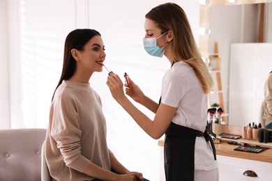 Makeup artist in protective mask working with woman indoors. Preventive measures during COVID-19 pandemic