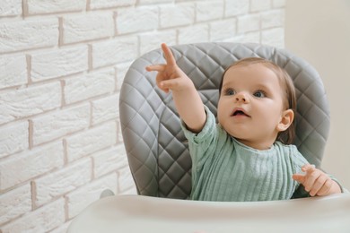 Cute little baby pointing at something in high chair indoors. Space for text