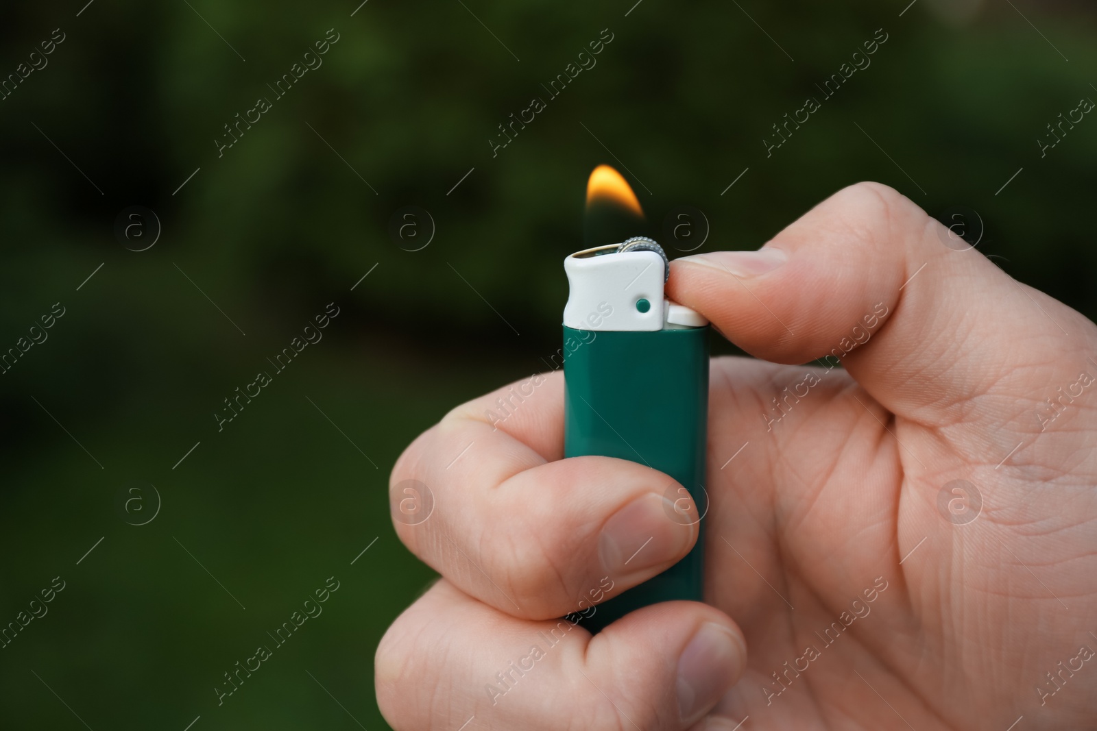 Photo of Man holding lighter with burning flame outdoors, closeup. Space for text