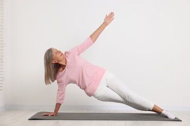 Photo of Senior woman practicing yoga on mat near white wall