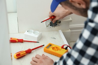 Electrician with screwdriver repairing power socket indoors, closeup