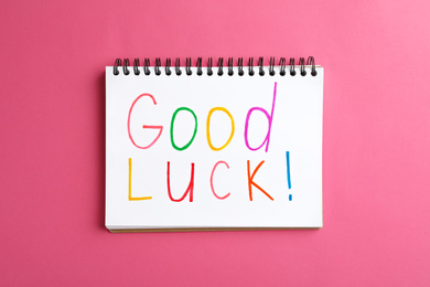 Photo of Notebook with phrase GOOD LUCK on pink background, top view