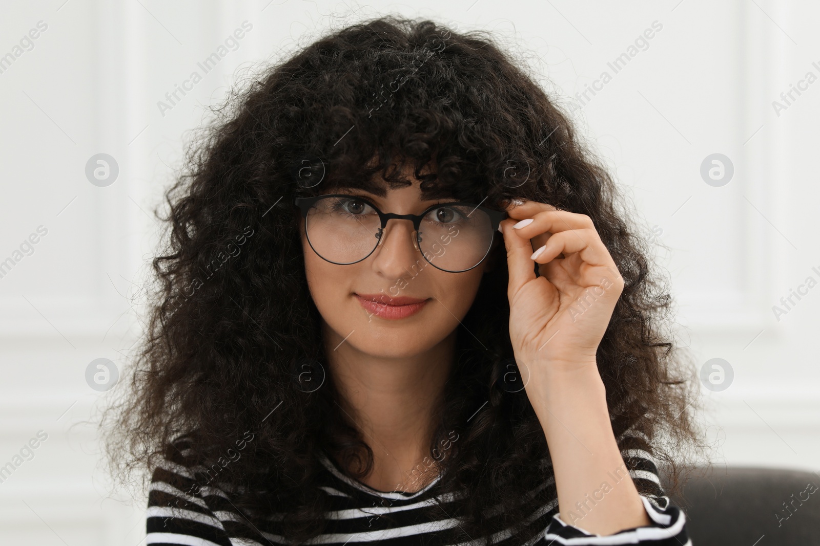 Photo of Portrait of beautiful woman with curly hair sitting on armchair indoors. Attractive lady looking at camera