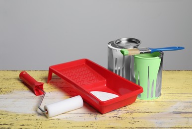 Photo of Cans of paints, brush, roller and tray on yellow wooden table