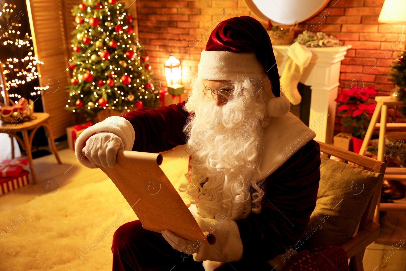 Photo of Santa Claus in glasses reading wish list indoors