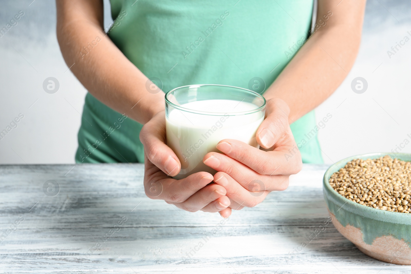 Photo of Woman holding glass of hemp milk near table, closeup