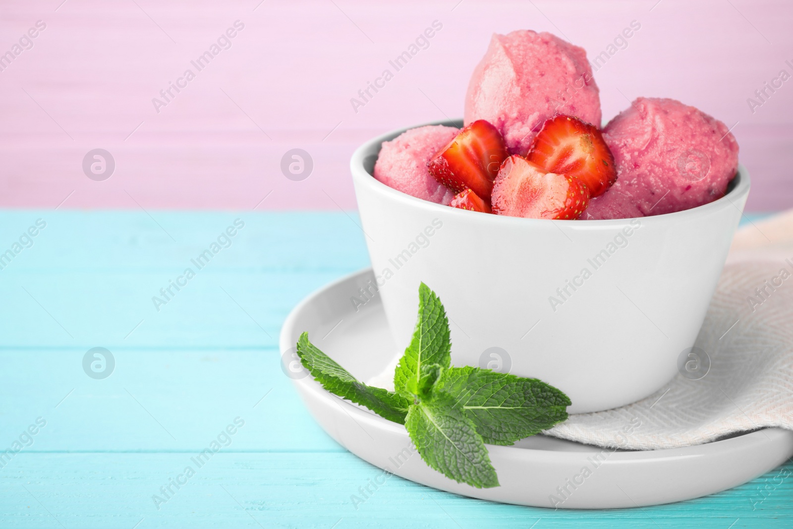 Photo of Bowl with delicious strawberry ice cream on light blue wooden table, space for text