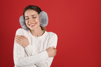 Happy woman wearing warm earmuffs on red background, space for text