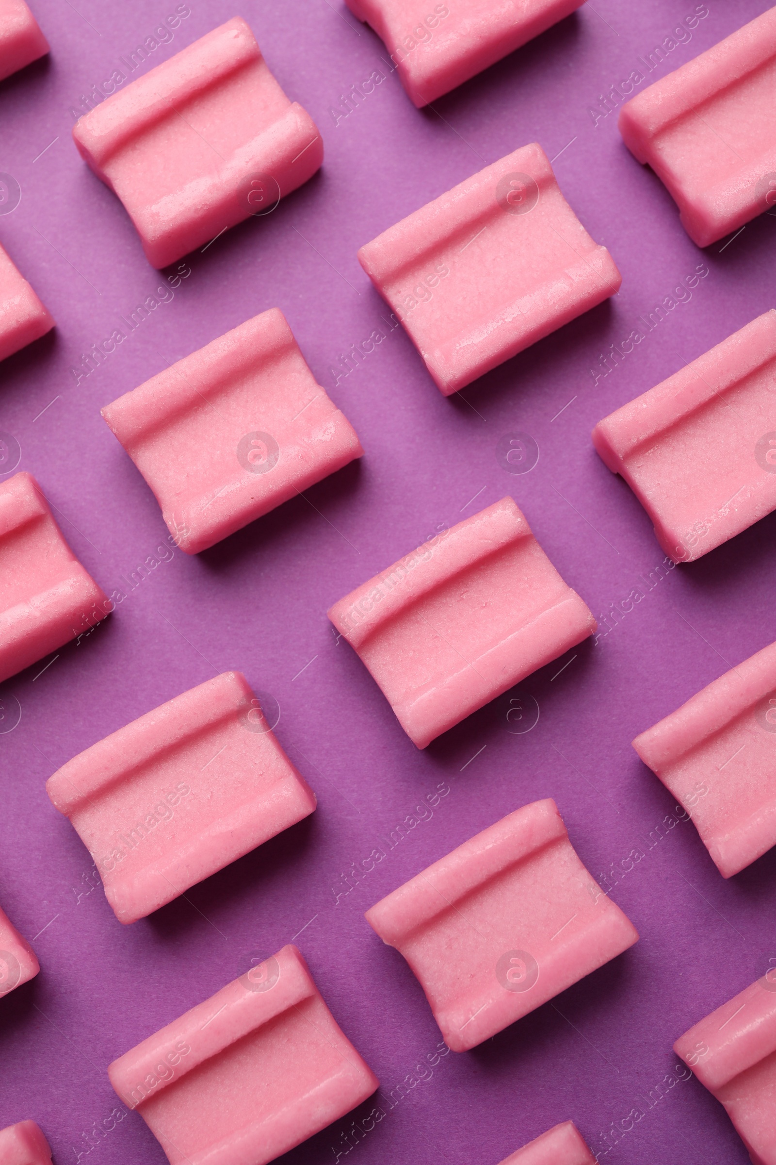 Photo of Tasty pink chewing gums on purple background, flat lay