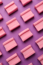 Photo of Tasty pink chewing gums on purple background, flat lay