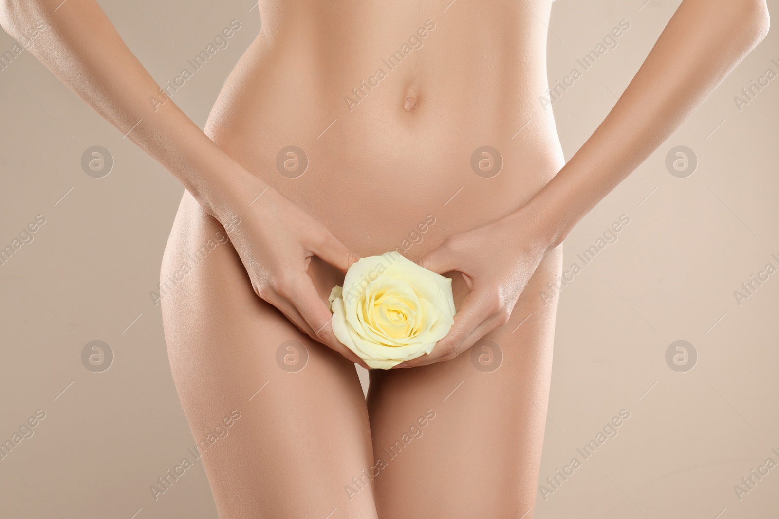 Photo of Woman with flower showing smooth skin after Brazilian bikini epilation on beige background, closeup. Body care concept
