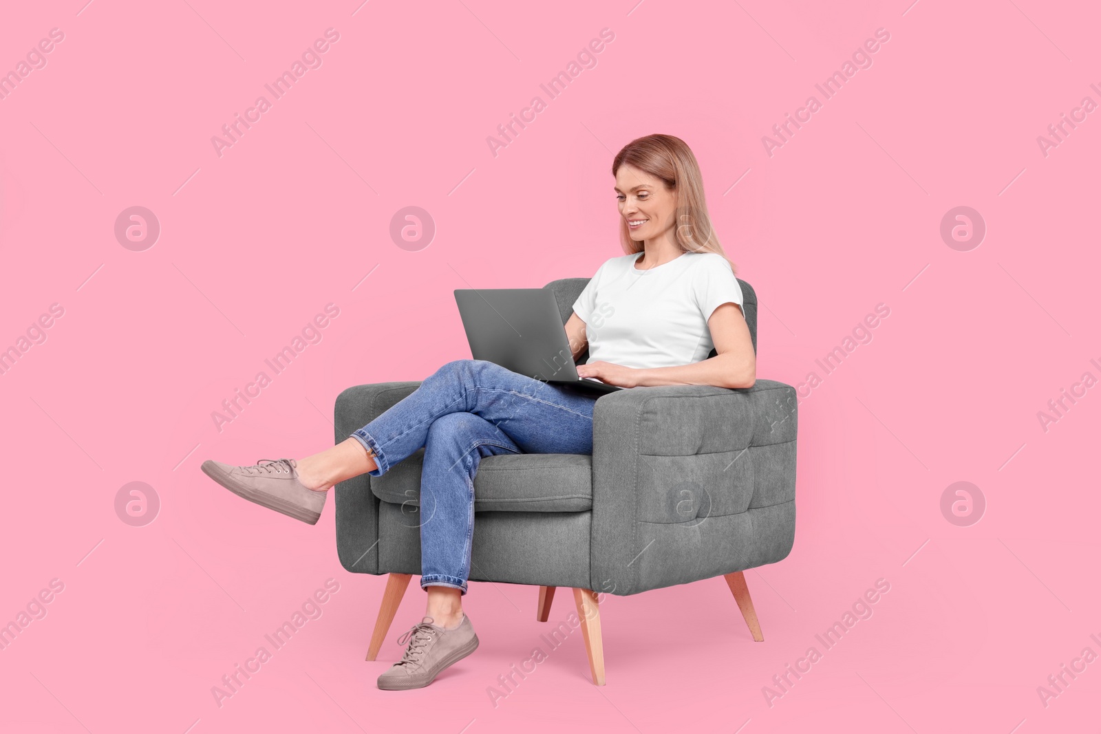 Photo of Happy woman with laptop sitting in armchair against pink background