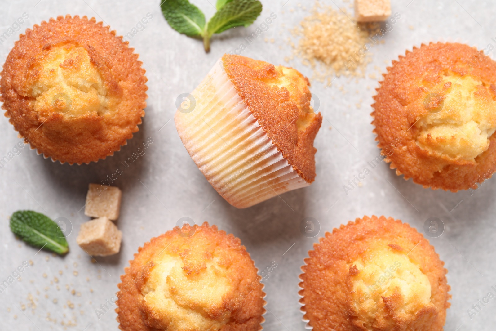 Photo of Delicious sweet muffins and brown sugar on light grey textured table, flat lay