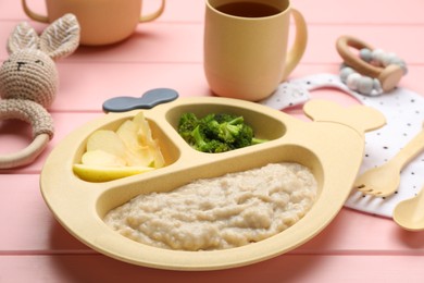 Photo of Plastic dishware with healthy baby food on pink wooden table, closeup
