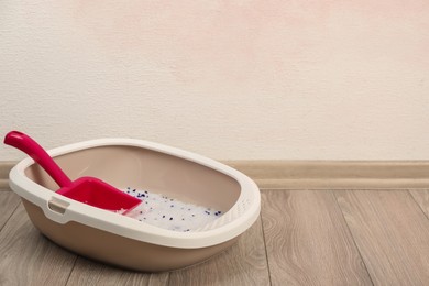 Photo of Cat tray with crystal litter and scoop on floor near pink wall. Space for text