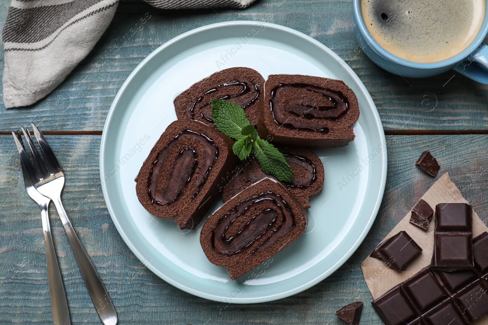 Photo of Tasty chocolate cake roll with cream and mint on blue wooden table, flat lay