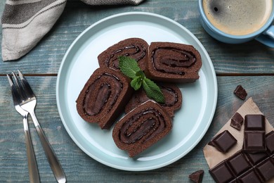 Tasty chocolate cake roll with cream and mint on blue wooden table, flat lay