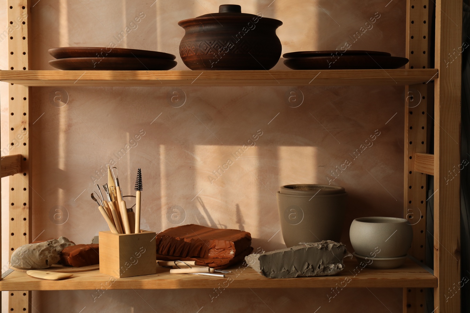 Photo of Set of different crafting tools and clay dishes on wooden rack in workshop