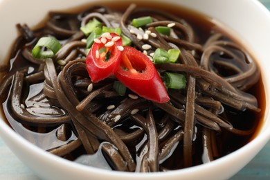 Photo of Tasty soup with buckwheat noodles (soba), chili pepper, green onion and sesame in bowl, closeup