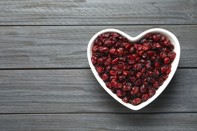 Photo of Heart shaped bowl with cranberries on wooden background, top view with space for text. Dried fruit as healthy snack