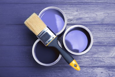 Image of Tin cans with violet paints and brush on wooden background, top view