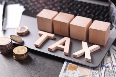 Word Tax made of wooden letters, cubes, laptop, banknotes and coins on grey table