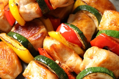 Delicious chicken shish kebabs with vegetables as background, closeup